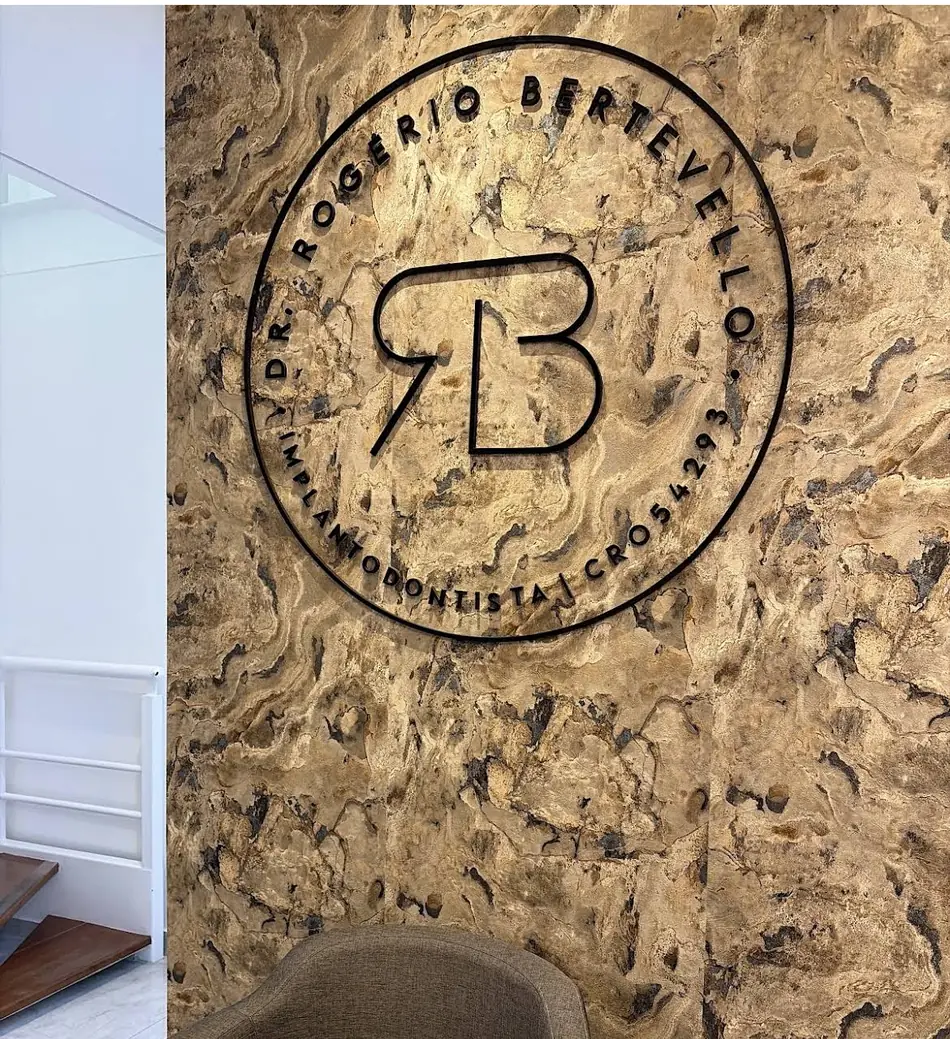 Recepção da clínica do Dr. Rogério Bertevello, com o selo da marca na parede de travertino